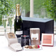 The Luxury Champagne Pamper Gift Box. A gift arrangement featuring a bottle of champagne, two fluted glasses, a box of chocolates, and gourmet snacks. There are also a pair of cozy socks and a decorative box labeled "DUBLIN HERBALISTS." The items are presented on a white surface with greenery visible in the background. The Luxury Champagne Pamper Gift Box. A gift arrangement featuring a bottle of champagne, two fluted glasses, a box of chocolates, and gourmet snacks. There are also a pair of cozy socks and a decorative box labeled "DUBLIN HERBALISTS." The items are presented on a white surface with greenery visible in the background.